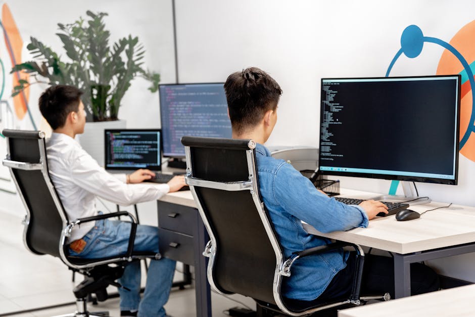 Two male developers at desks programming in a modern office workspace with large monitors
